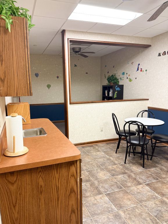 A small kitchen area with a sink and counter, a round table with chairs, and a doorway to another room.