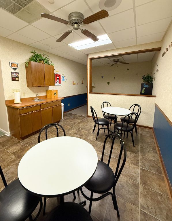Interior view of a breakroom with tables, chairs, a sink, and a small kitchen area.