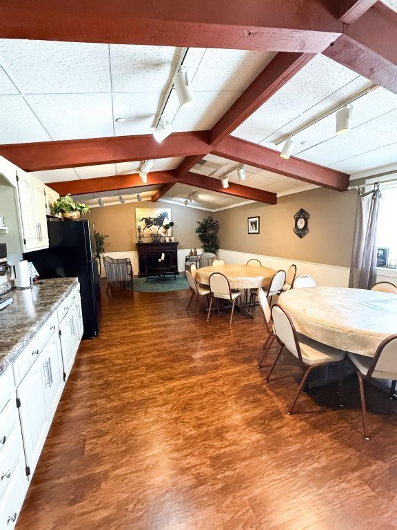 Interior view of a community room with tables, kitchen, fireplace, and exposed wooden beams.