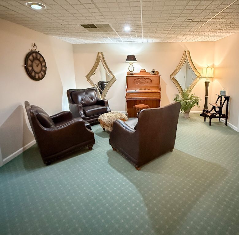 Cozy room with leather chairs, antique piano, gold mirrors, and a grandfather clock.