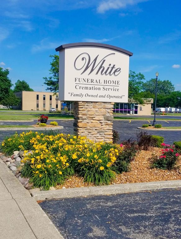 Sign for White Funeral Home, with stone base and flowers, on a sunny day.