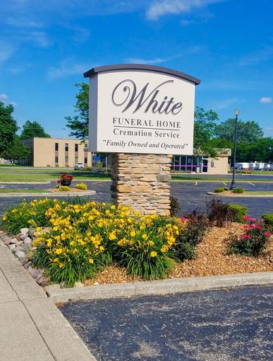 Sign for White Funeral Home, with stone base and flowers, on a sunny day.