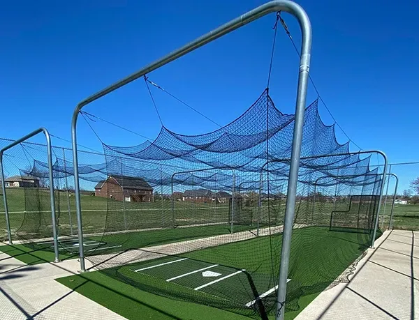 Baseball batting cage, metal frame with netting, on artificial turf, clear blue sky.