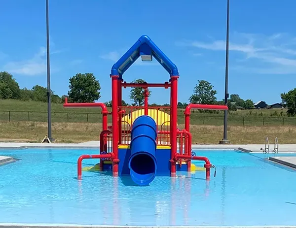 Blue and red water slide structure in a pool, under a bright blue sky.