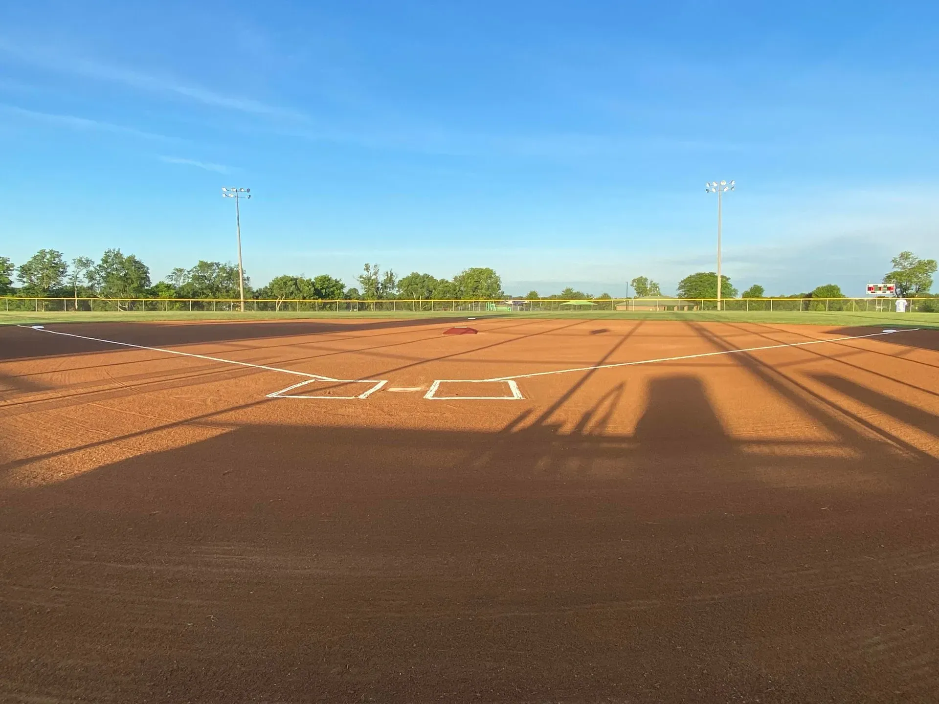 Baseball field under a blue sky, with infield dirt and white base lines.