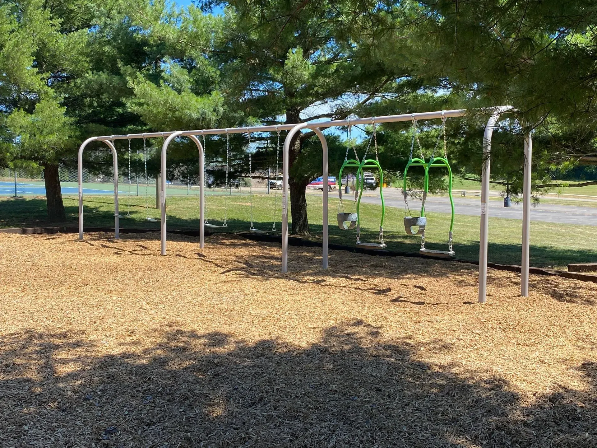 Swing set with green swings, located in a park with wood chips on the ground.