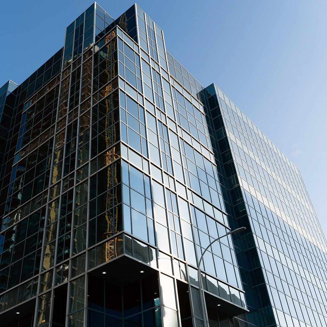 Glass-walled office building against a blue sky, reflecting the sky and surrounding buildings.