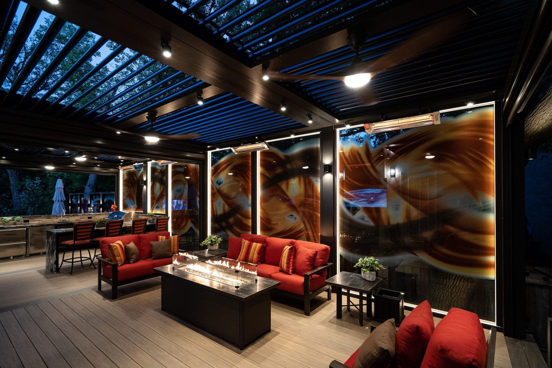 Outdoor living room with red sofas, fire pit, art panels, and pergola roof.