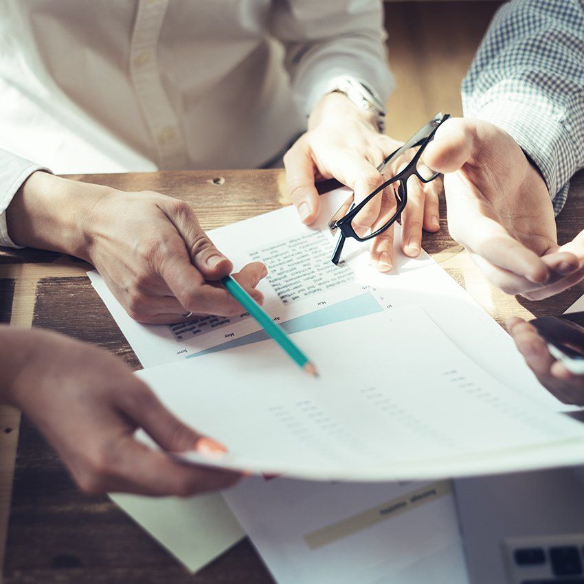 Hands pointing at documents during a business meeting. Glasses and pen are also visible.