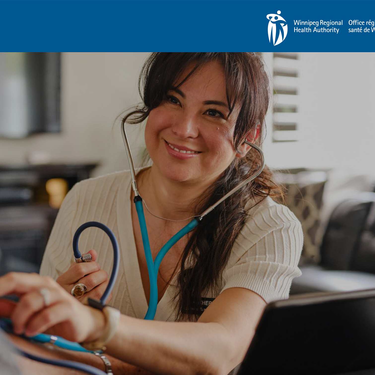 Woman with a stethoscope, smiling while examining someone's arm in a home setting.