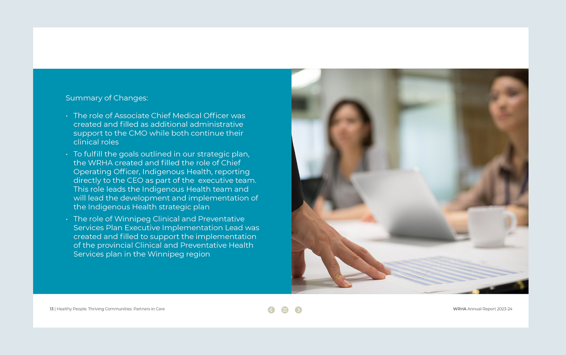 Person's hand pointing at documents on a table with colleagues in the background.