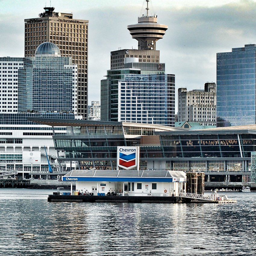 Chevron gas station on a barge in Vancouver harbor with city skyline in the background.