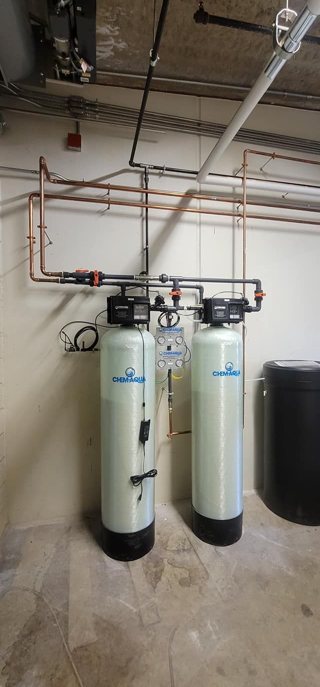 Two tall white water softener tanks with copper piping in a basement utility room