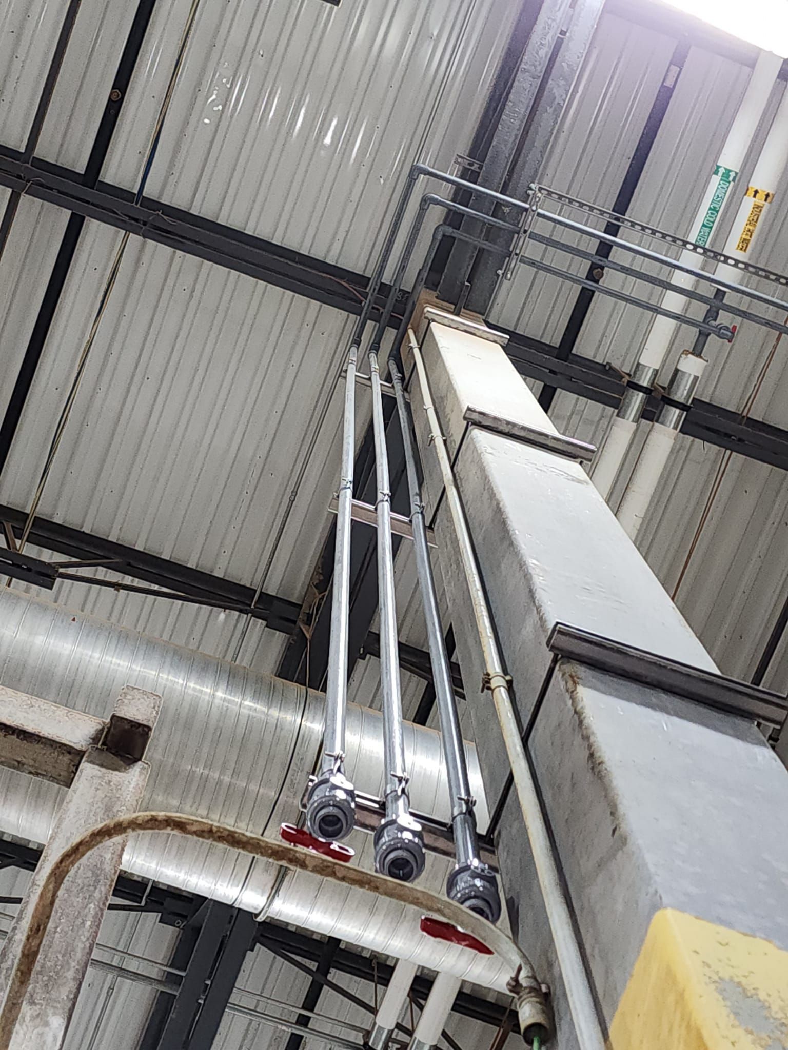 Industrial ceiling with metal beams, pipes, and a tall gray ventilation or duct system viewed from below