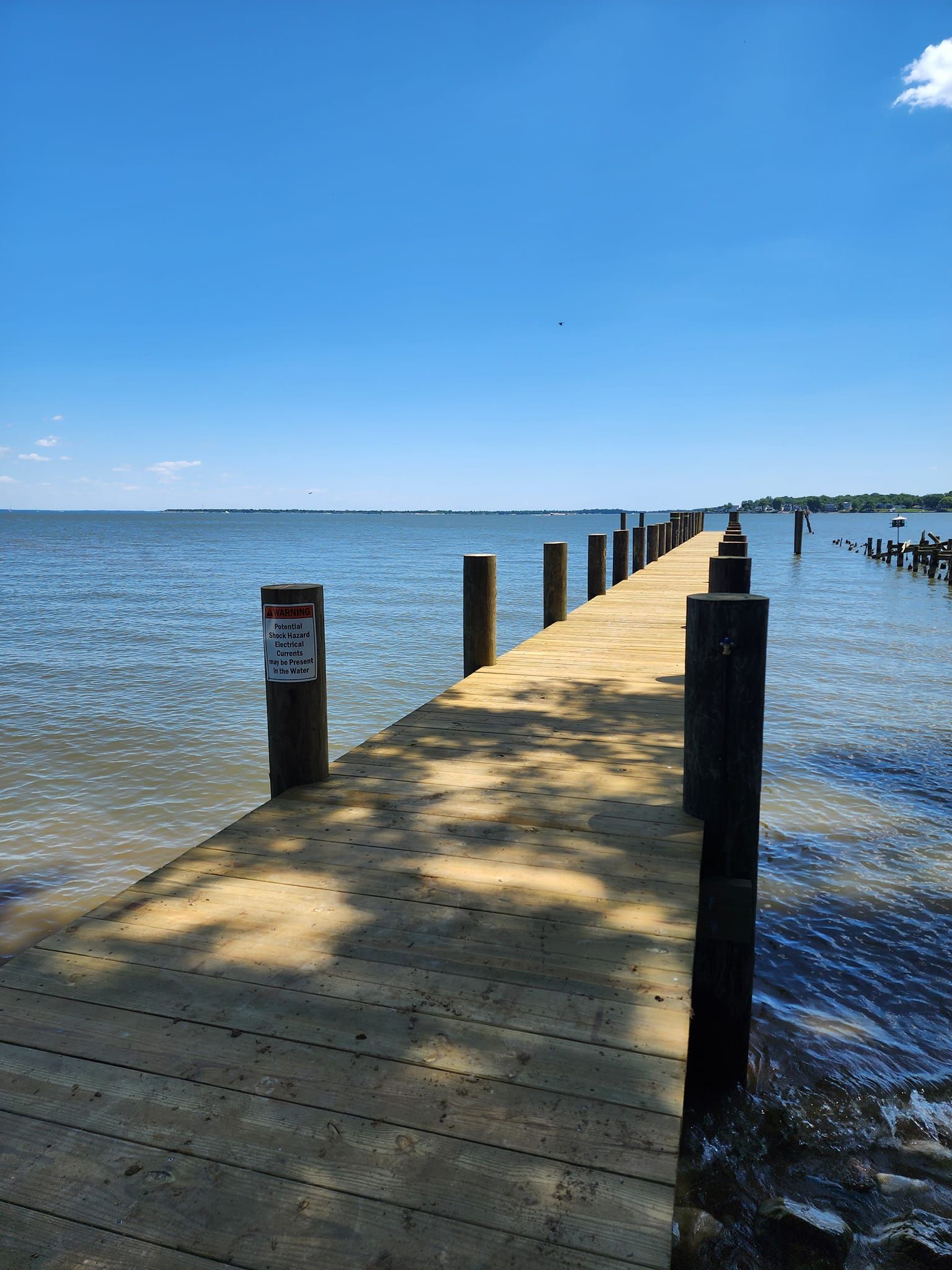Wooden pier stretching into calm blue water under a clear sky, with posts lining the walkway.