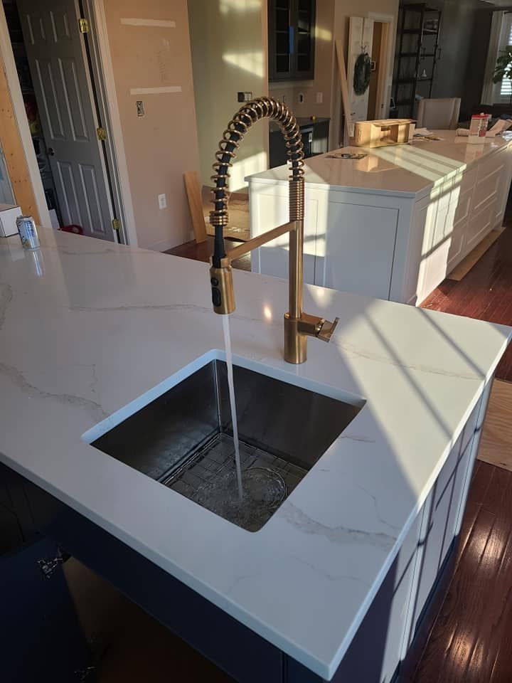 Modern kitchen island with a brass faucet and white countertops, featuring a built-in sink and dark wood floors.