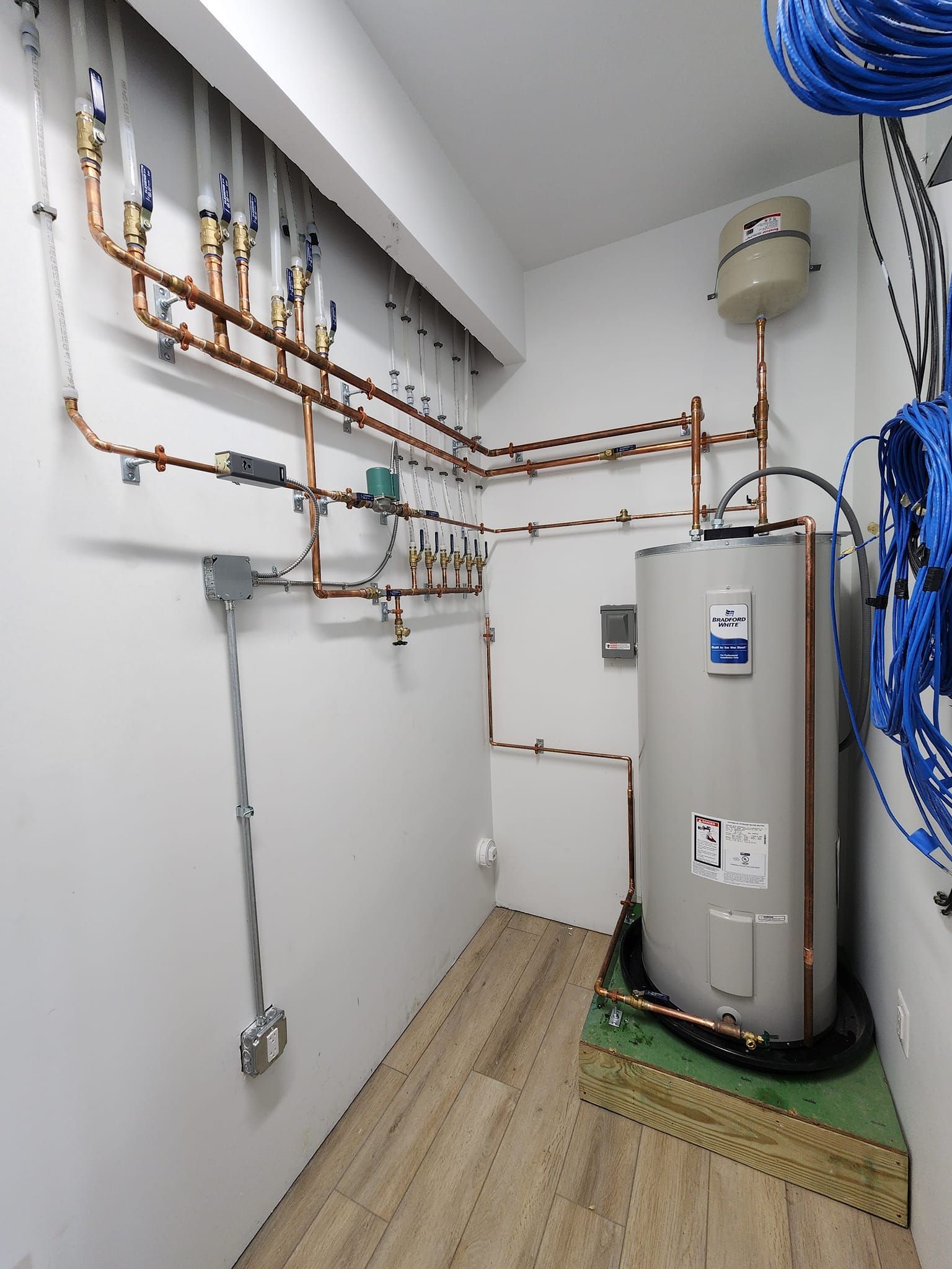 Utility room with copper pipes, wall-mounted water heater, and coiled blue hose on the right