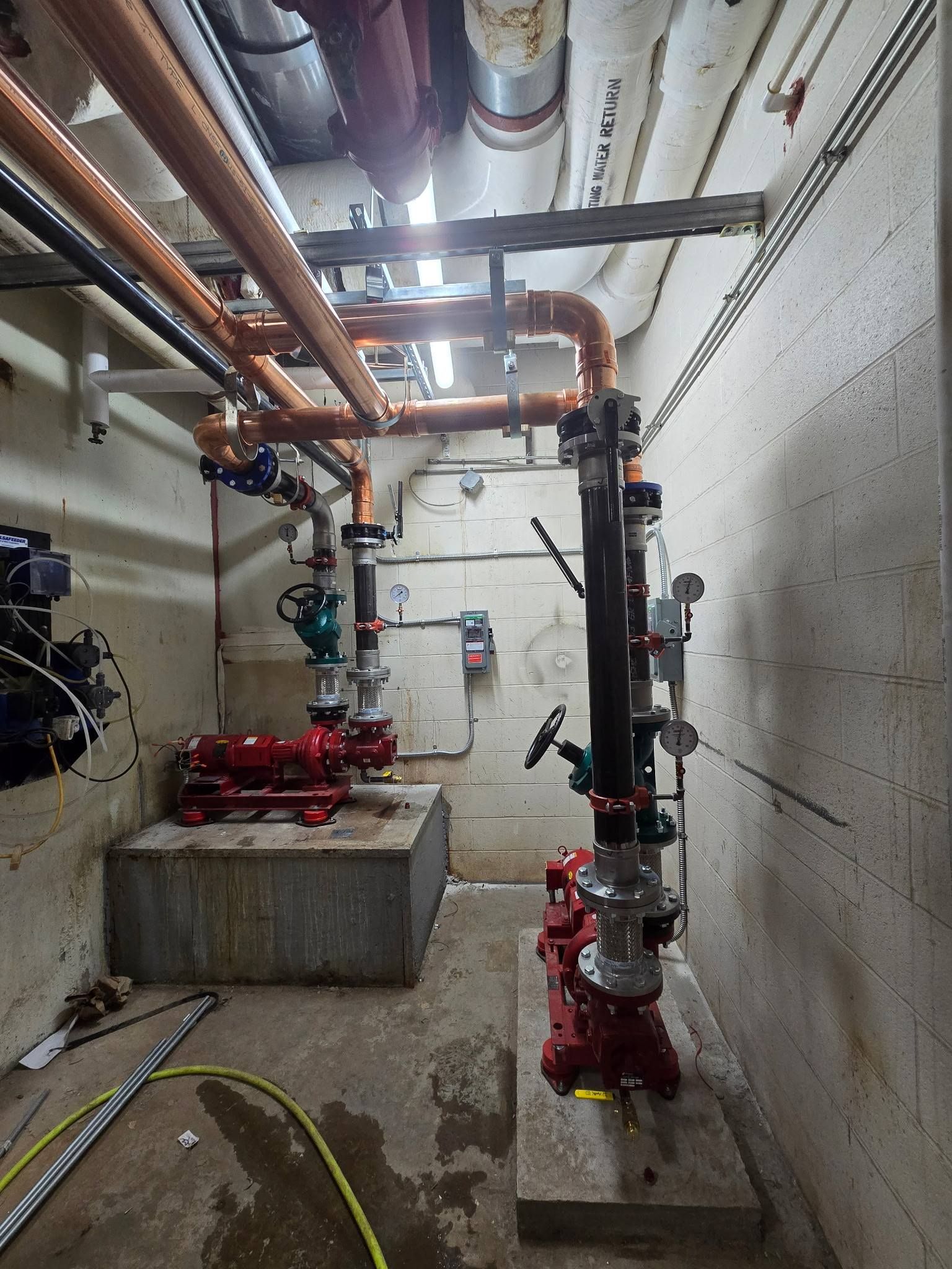 Industrial utility room with red and black pipes, valves, and pumps along concrete walls and floor.