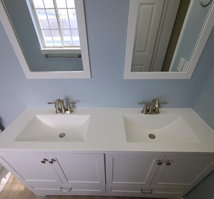 White double bathroom vanity with two sinks, mirrors, and chrome faucets against light blue walls.