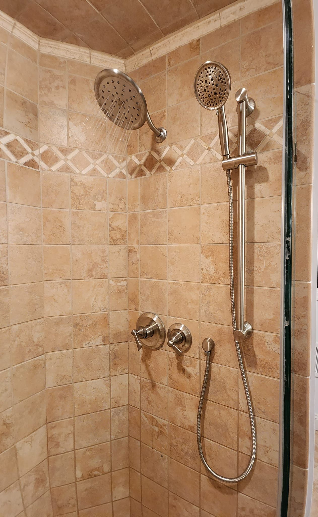 Tan tiled shower with two showerheads, metal controls, and a handheld shower hose.