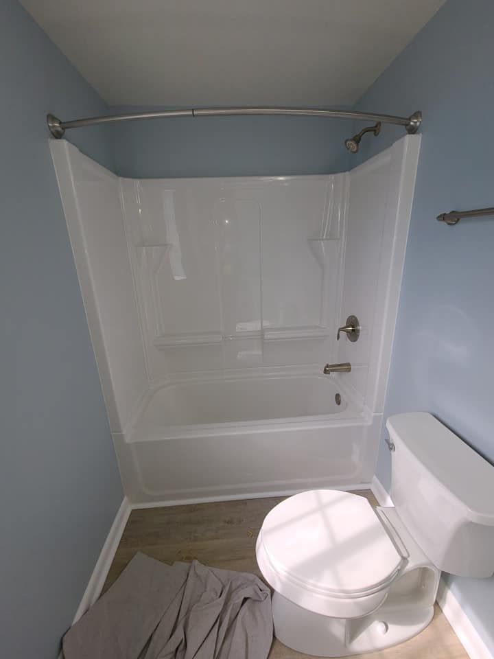 Small bathroom with a white tub and shower, toilet in front, and a gray towel on the floor.