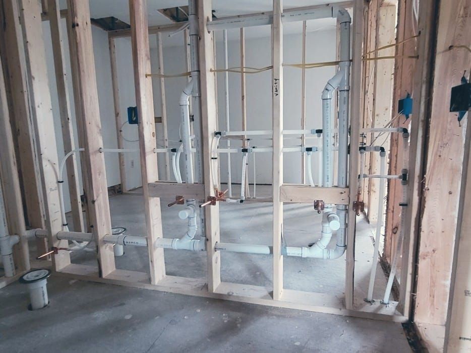 Framed bathroom under construction with exposed plumbing and unfinished drywall