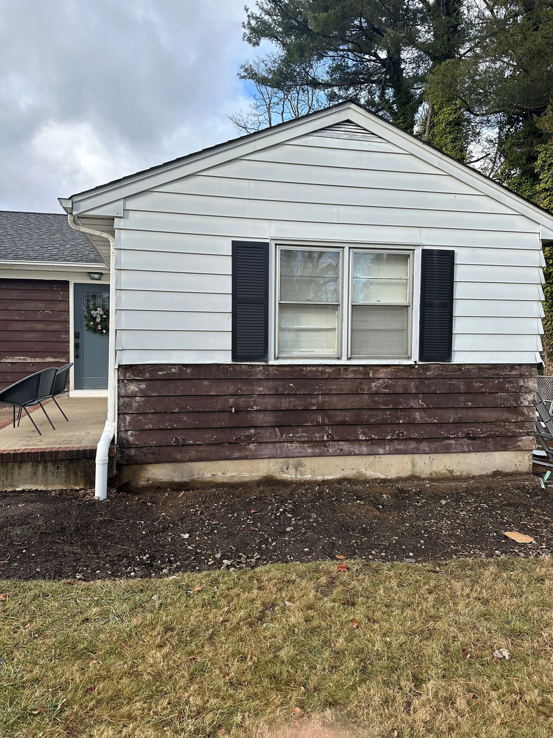 A house exterior with white upper siding, brown lower siding, black window shutters, and a grey door on a concrete porch.