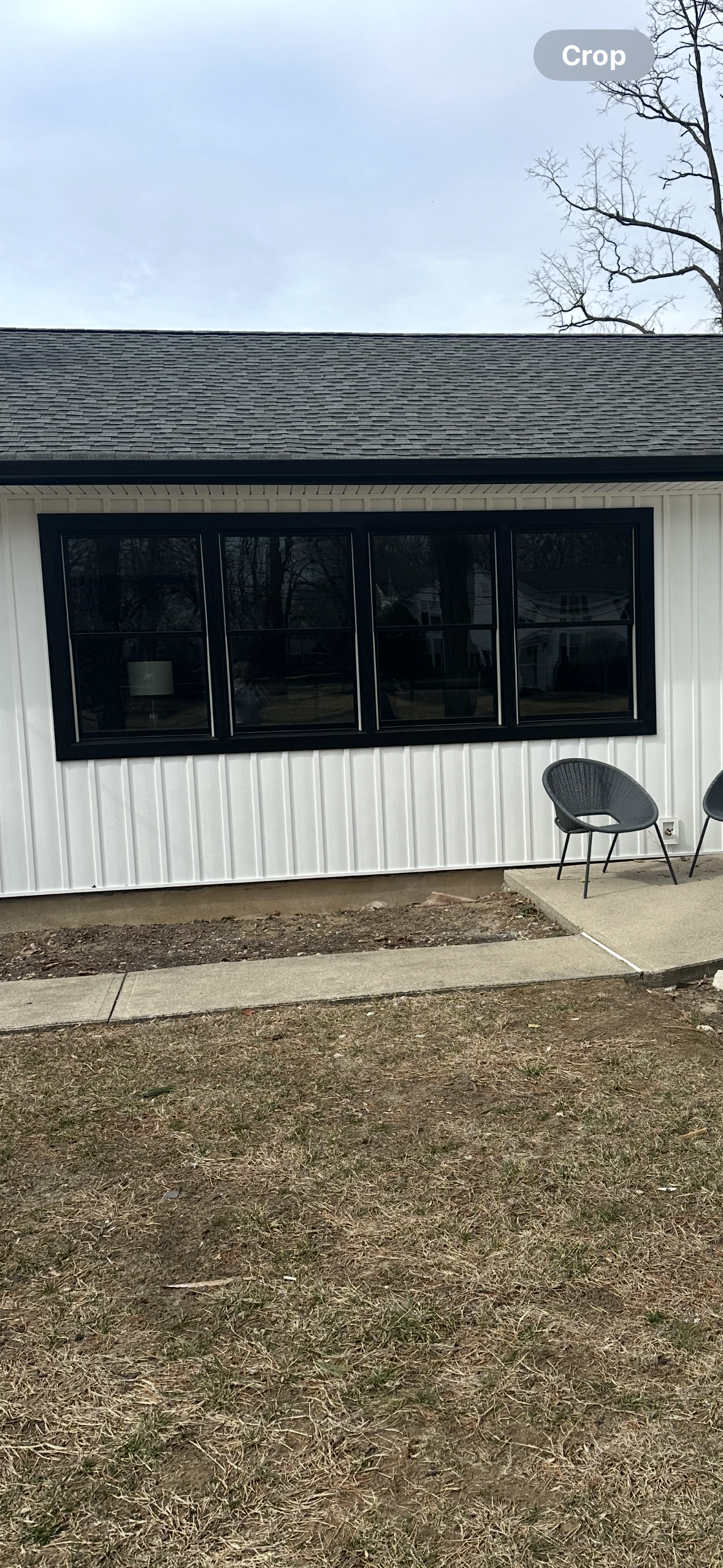 A white-sided house with a dark roof and a large, black-framed picture window above a gravel bed and concrete patio.