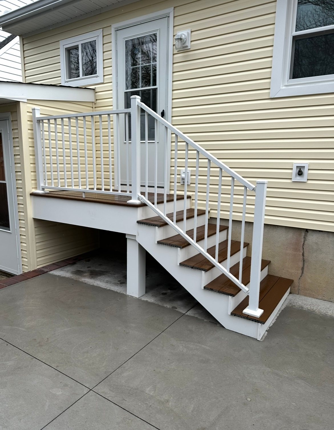 A set of wooden stairs with white railings leading up to a door on the side of a house with yellow siding.