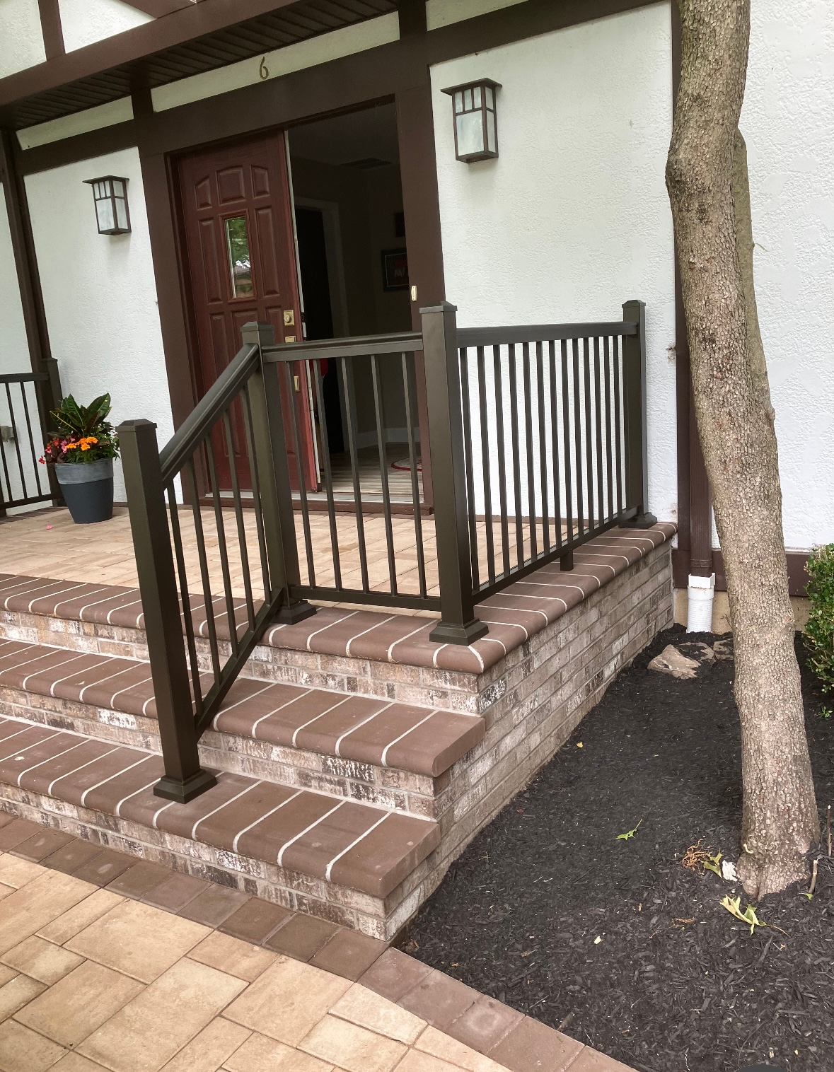 Front entrance with brick steps featuring brown treads, a metal handrail, and a potted plant by a doorway.