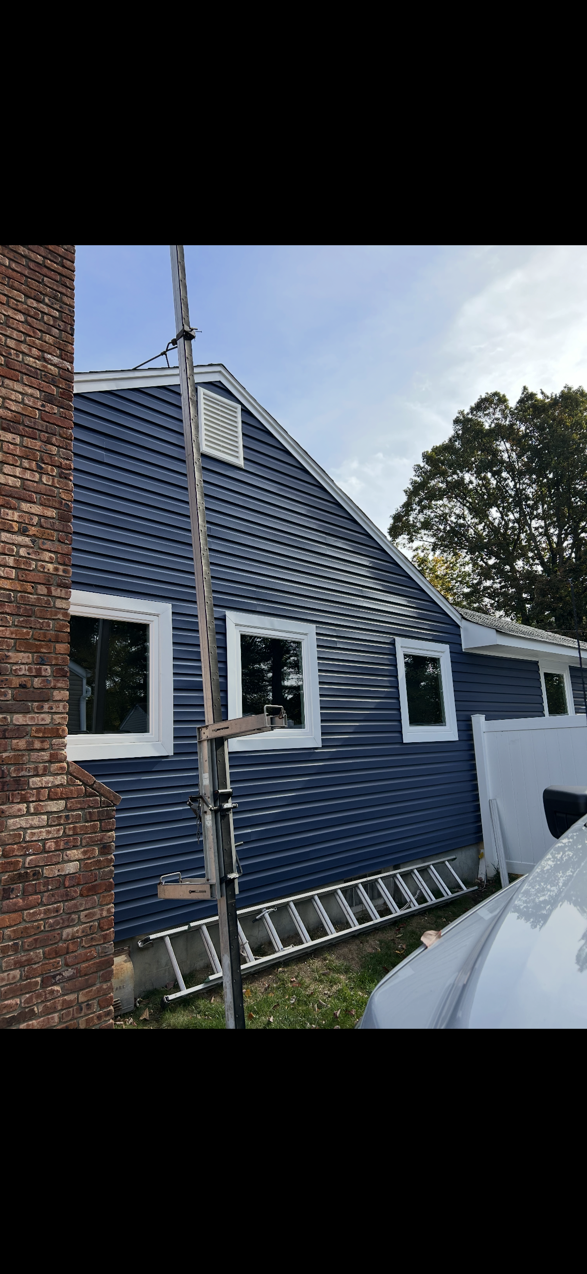A blue, wood-sided house exterior with white window trim and a tall metal antenna pole in the foreground.