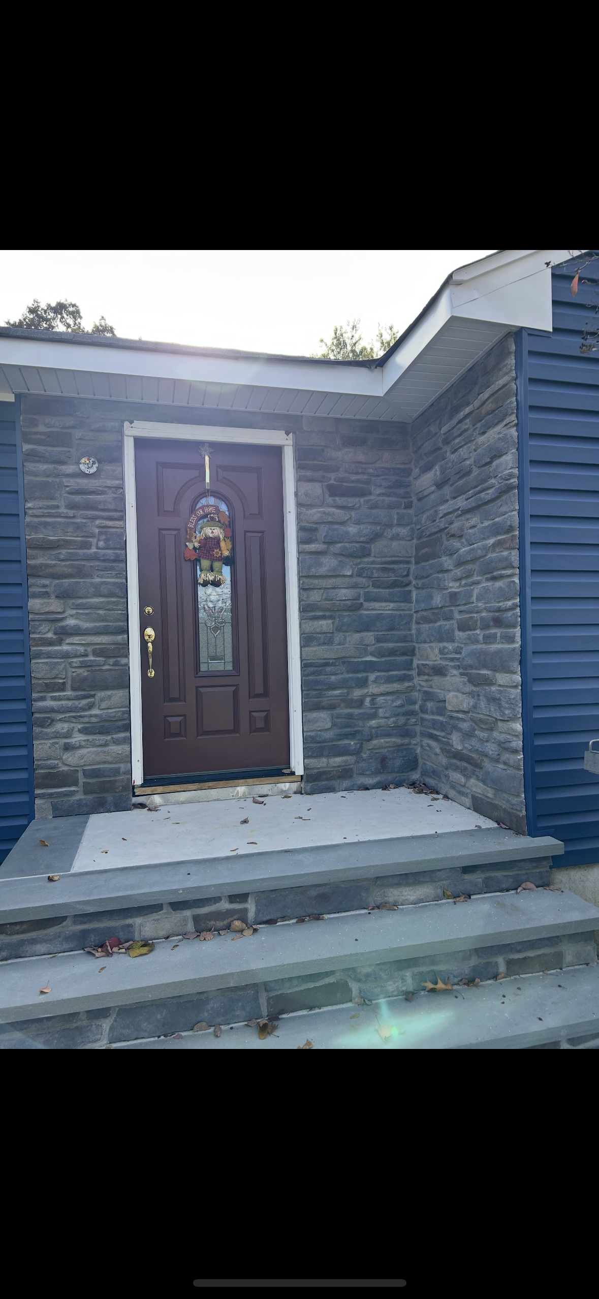 A front entry with a dark red door, stone facade walls, blue siding, and concrete steps with a white landing.
