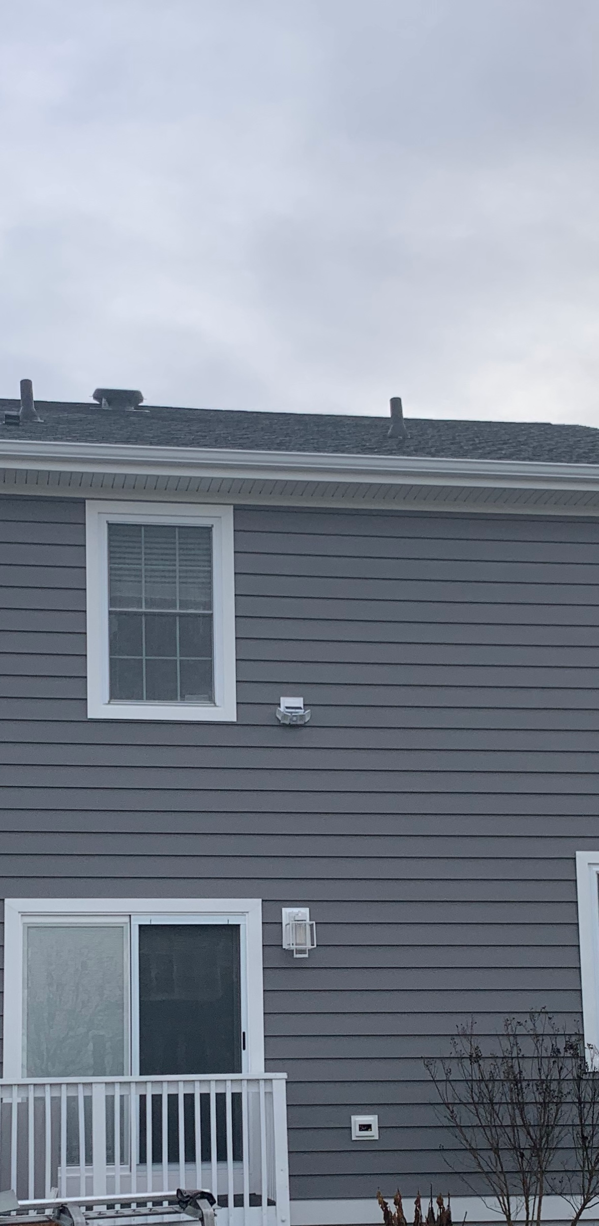 Gray siding on the exterior of a two-story home with windows and a sliding door leading to a balcony.