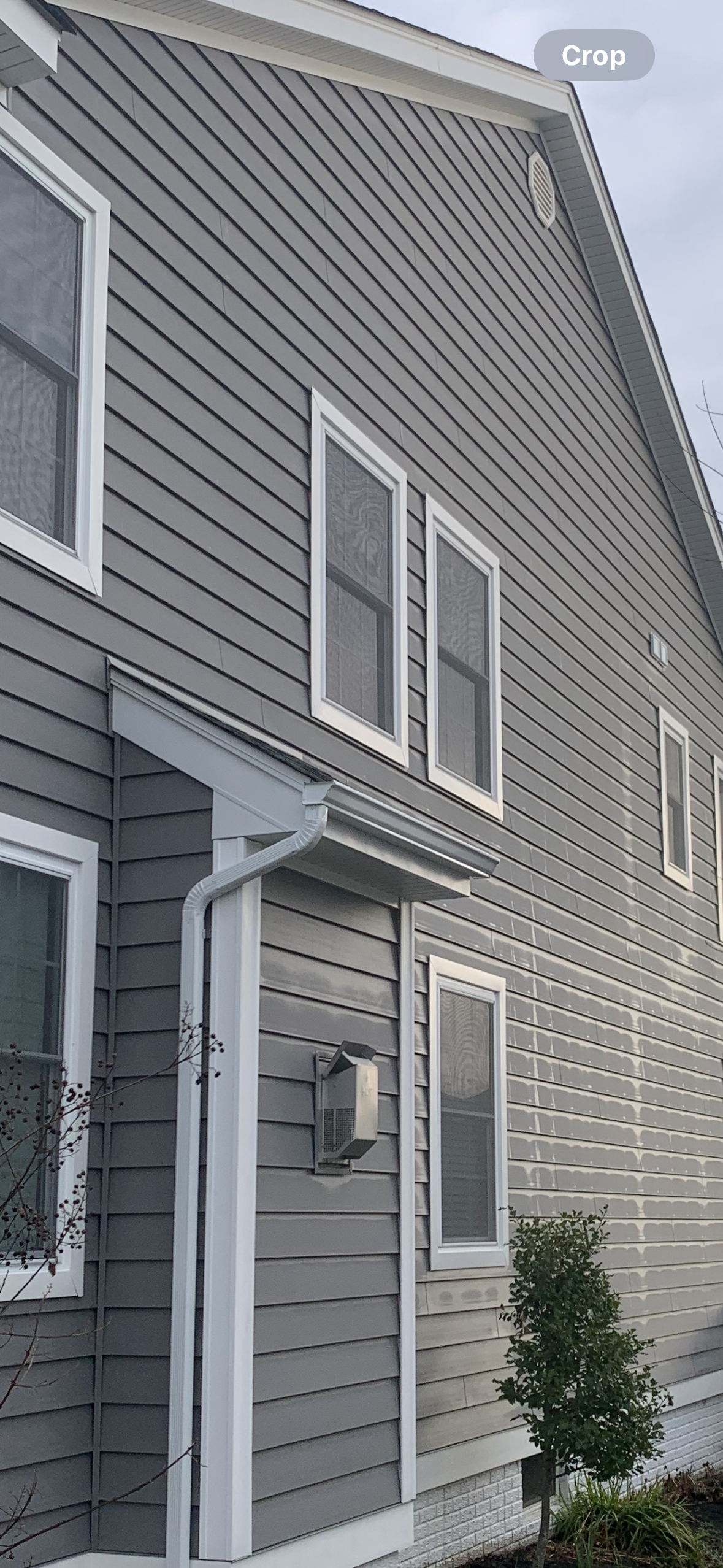 A side view of a gray-sided residential building with white window trim and a small entryway cover.