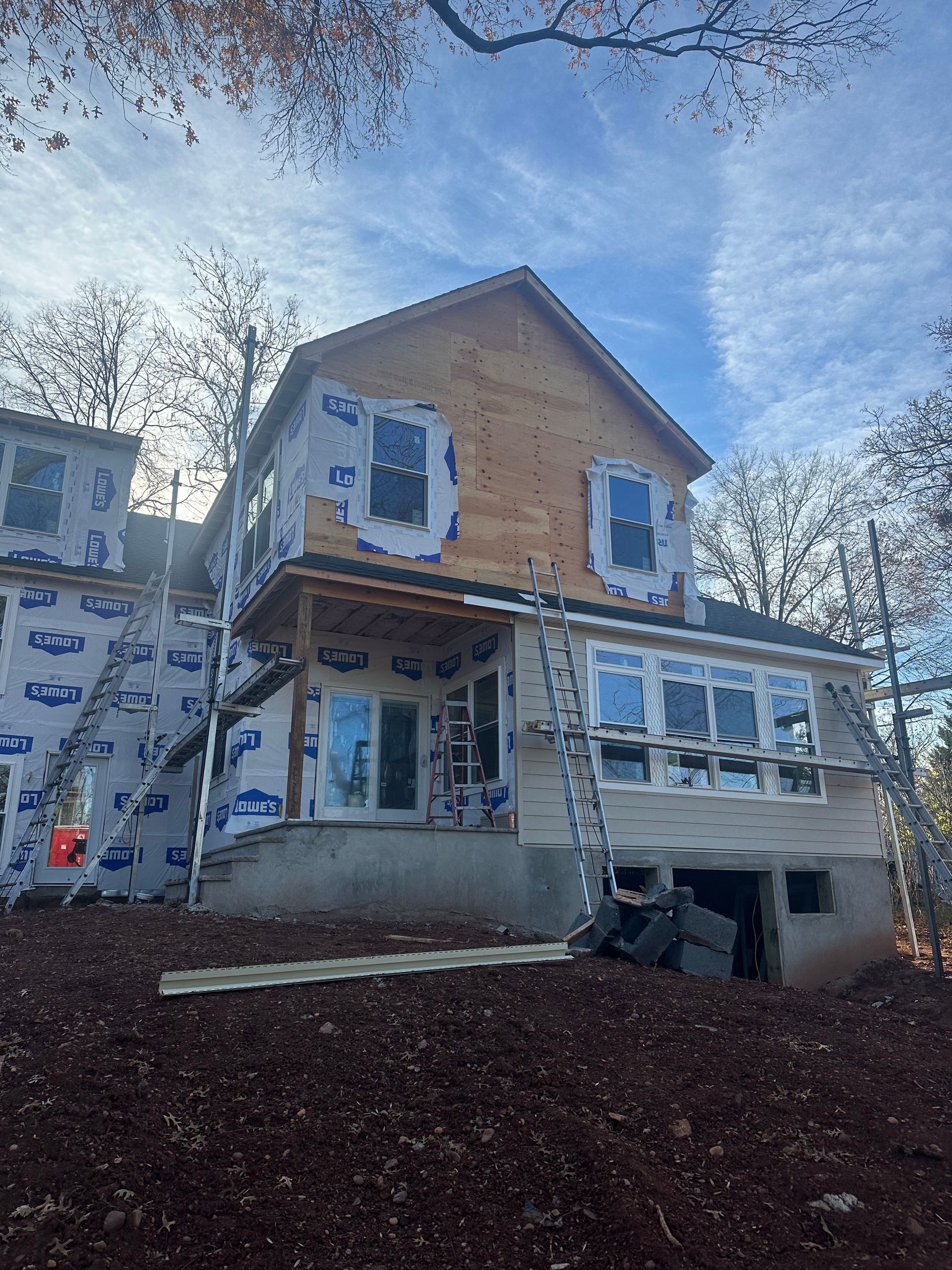 A house under construction with exposed plywood on the upper level and white house wrap covering the lower exterior walls.