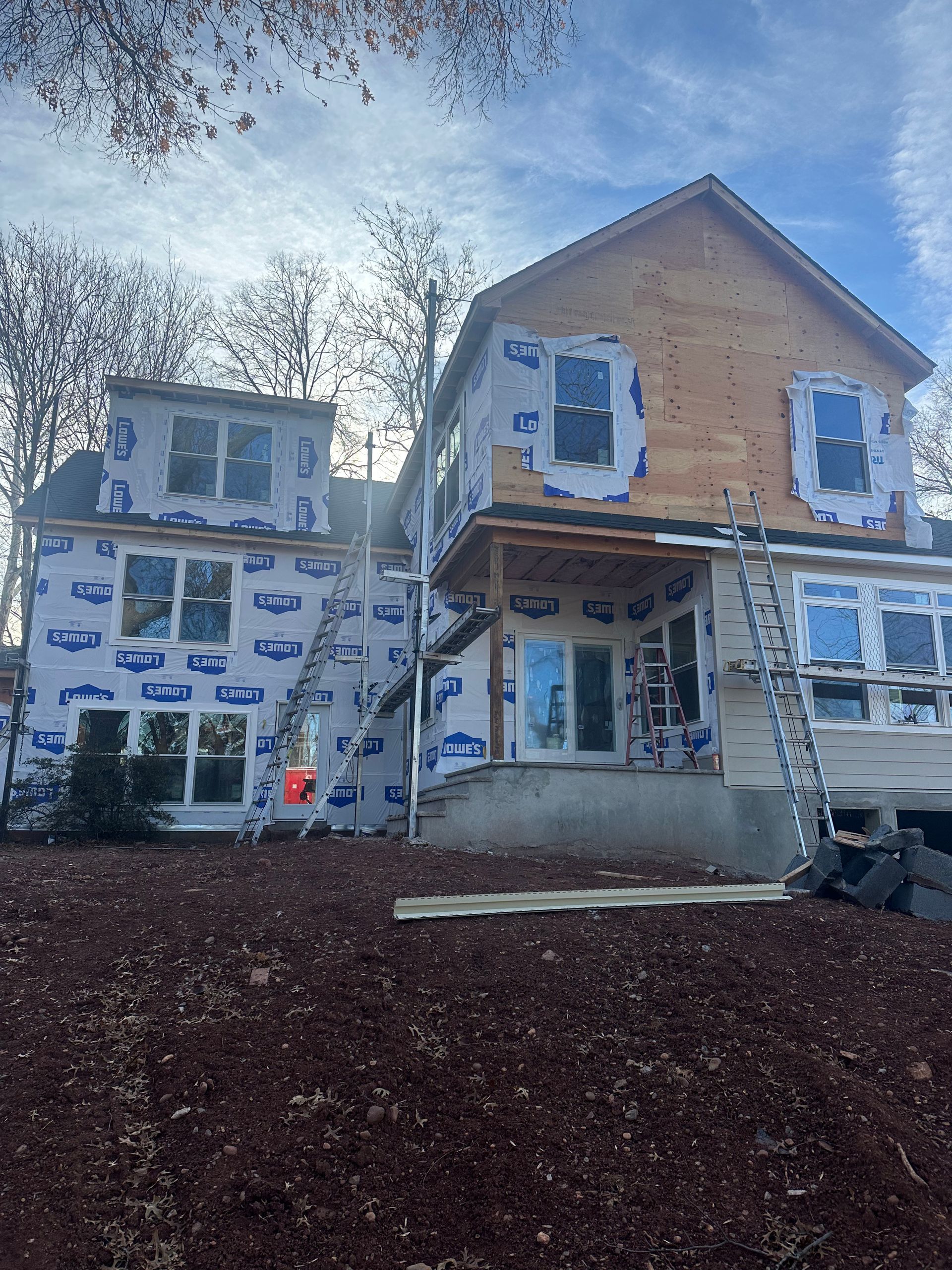 A residential home under construction, showing wood framing partially covered with white protective wrap and new windows.