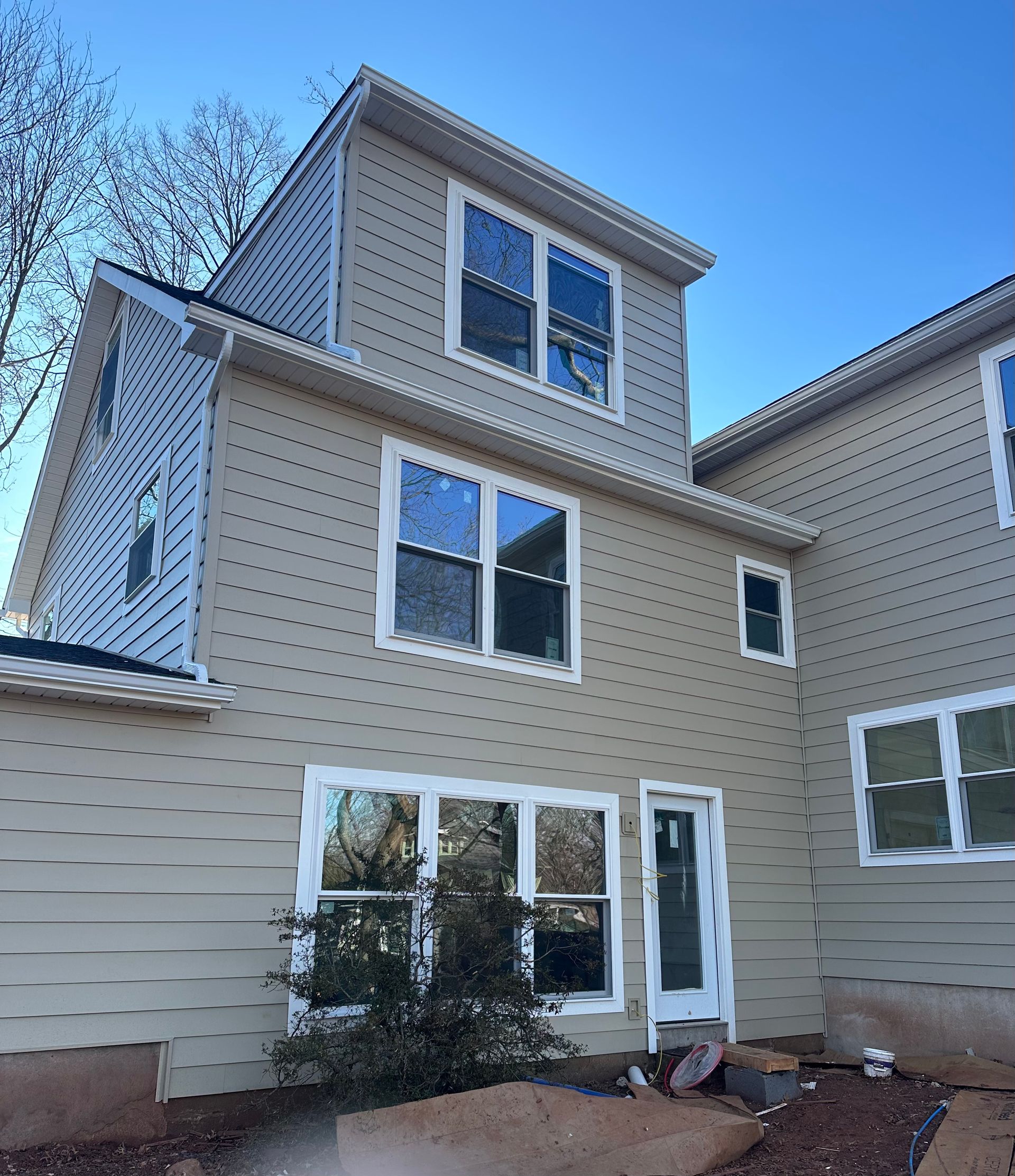 A three-story residential house under construction with light beige horizontal siding and white window frames.