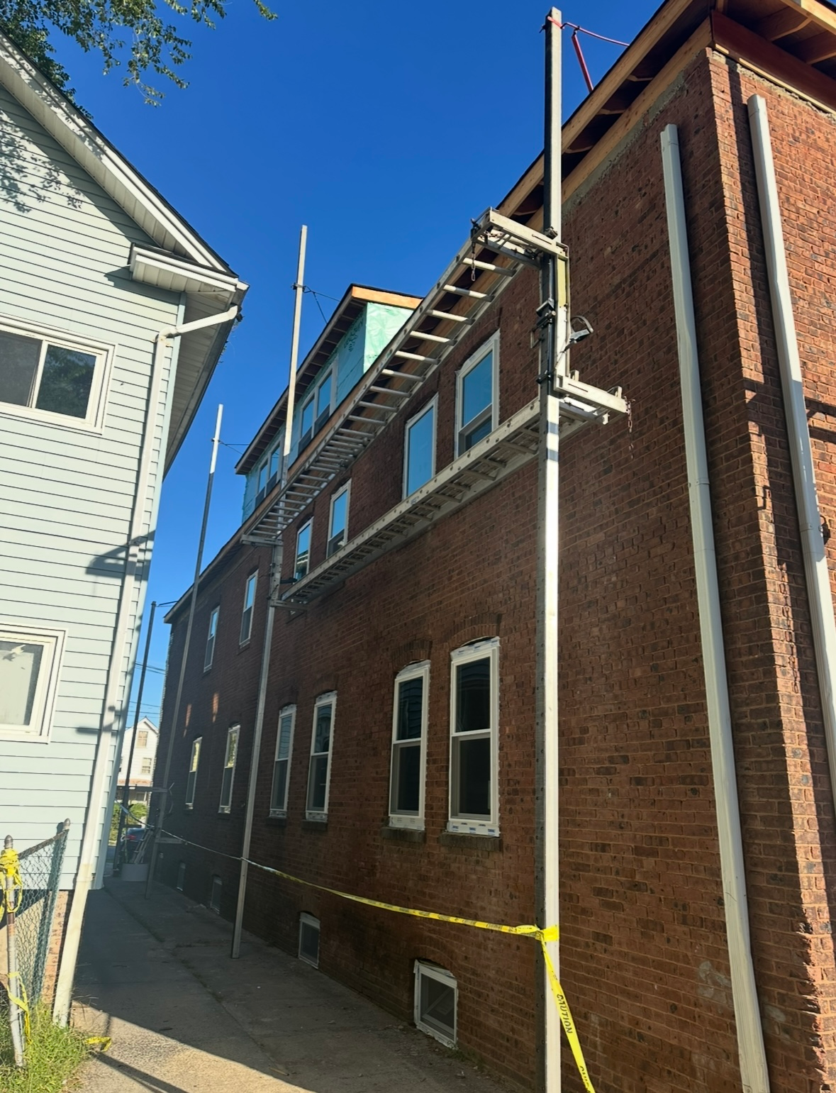 A brick building under repair with metal scaffolding poles installed along its exterior wall and yellow caution tape.