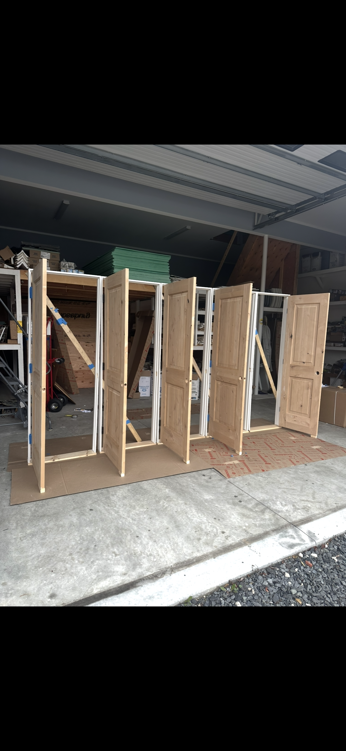 Five unfinished wooden interior doors stand upright in a row on cardboard mats in a garage.