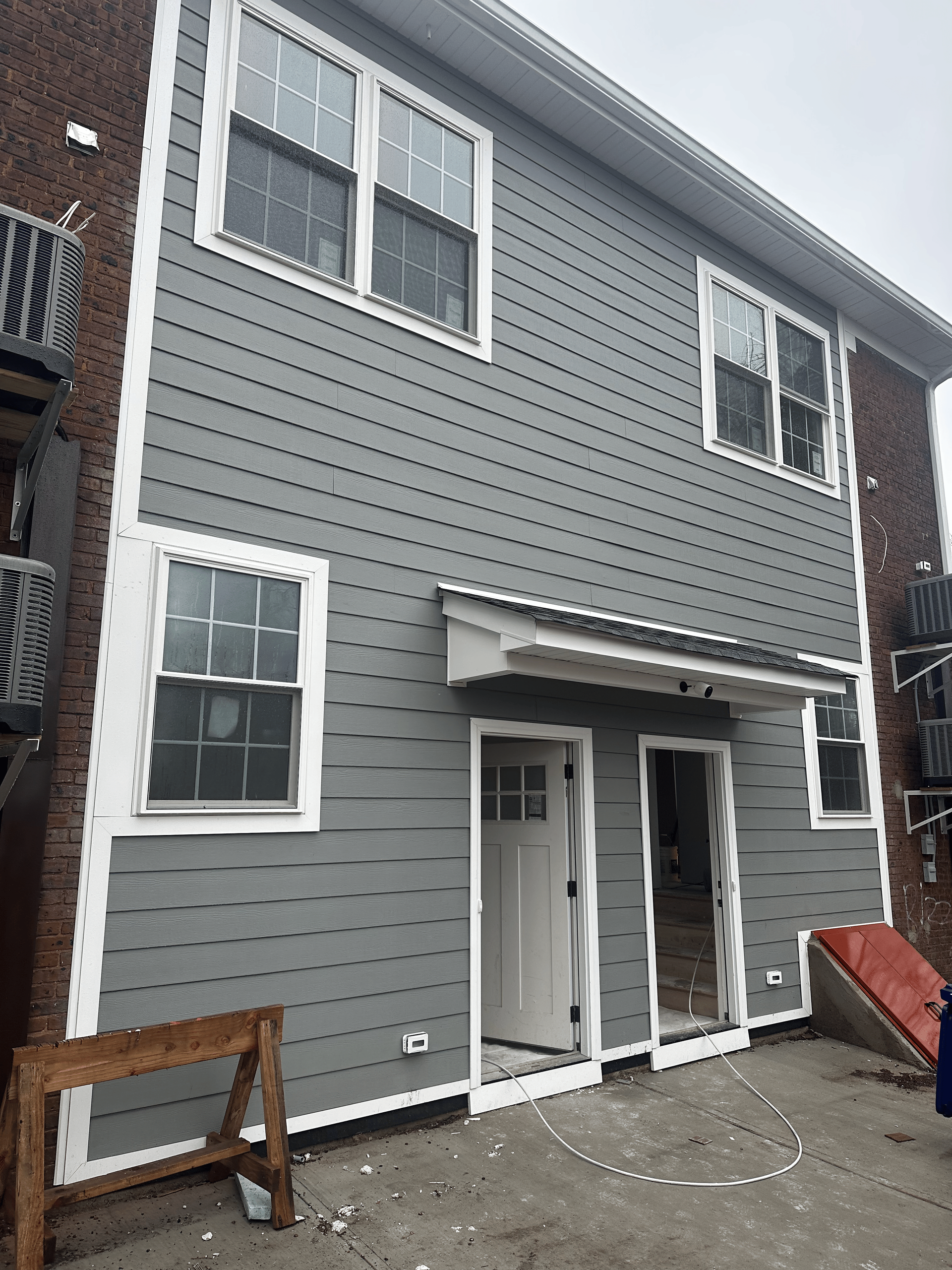 Gray, two-story house exterior featuring vinyl siding, white window trim, a small entryway overhang, and two open doors.