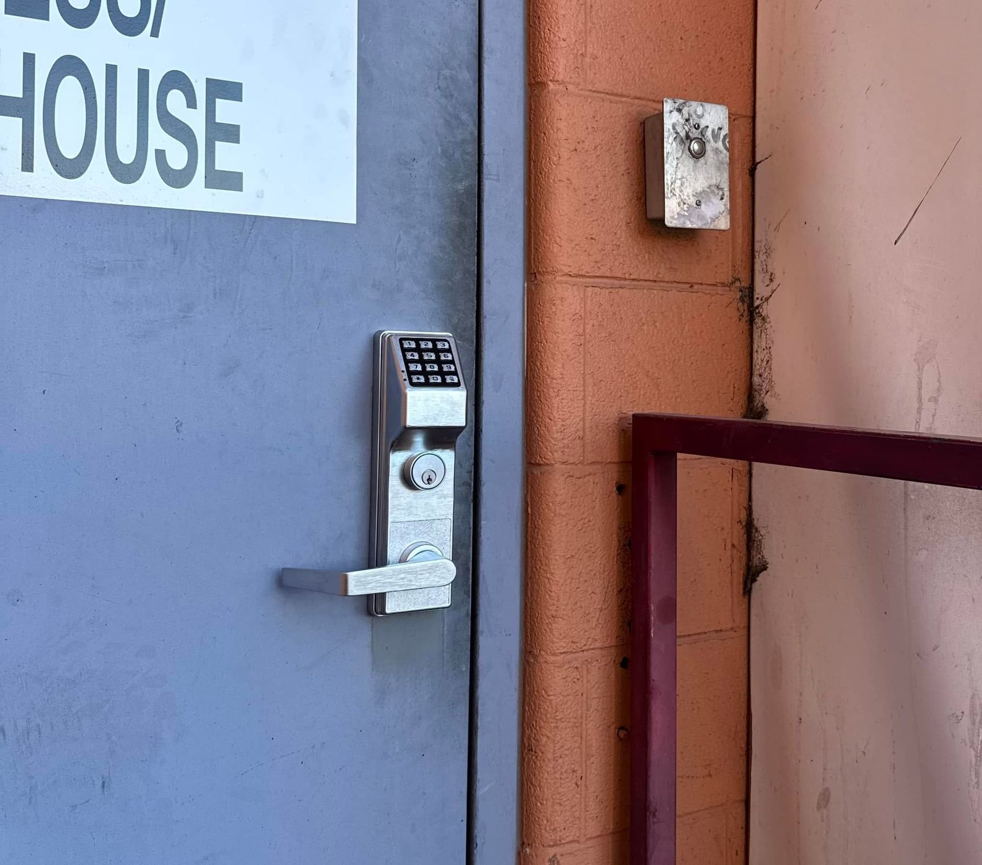 Keypad lock on a blue door beside a brick wall and metal railing