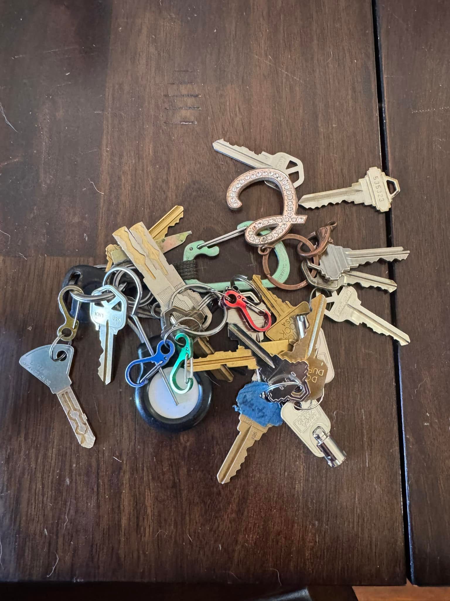A pile of assorted keys on a dark wooden table, including silver, gold, and blue keychain keys.