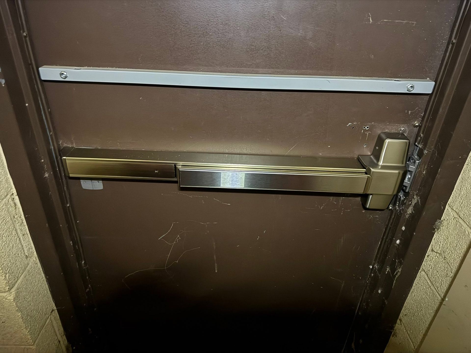 Brown door with a silver horizontal push bar and a door closer arm above it