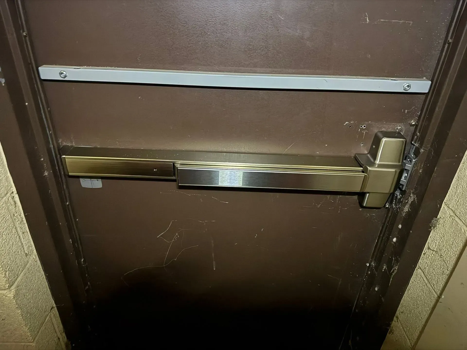 Close-up of a brown door with a metal push bar and a horizontal white safety bar.