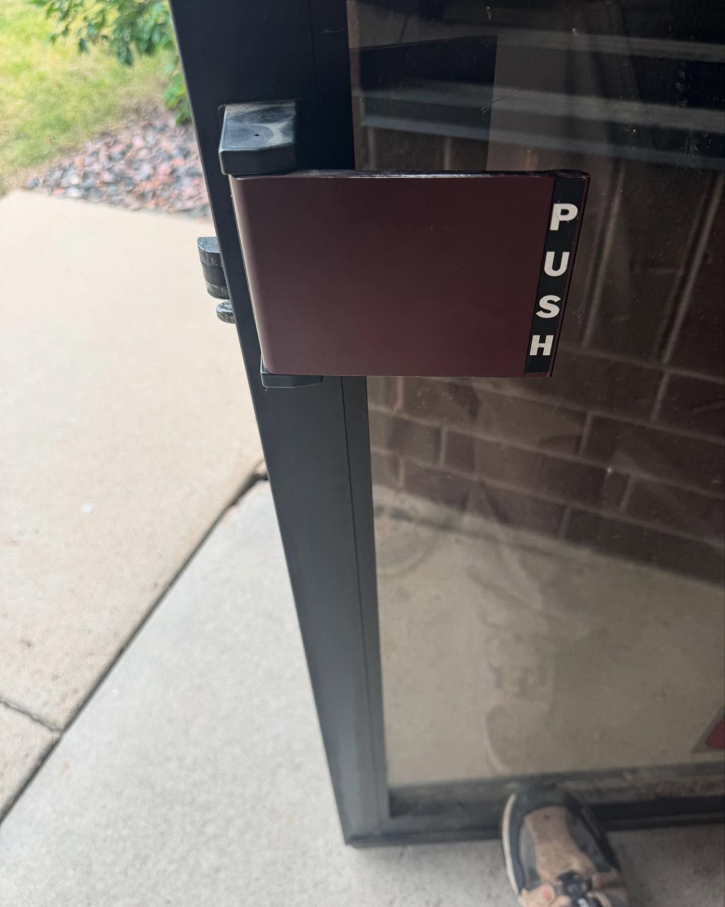 Glass door with a black push bar and a person’s shoe at the bottom edge