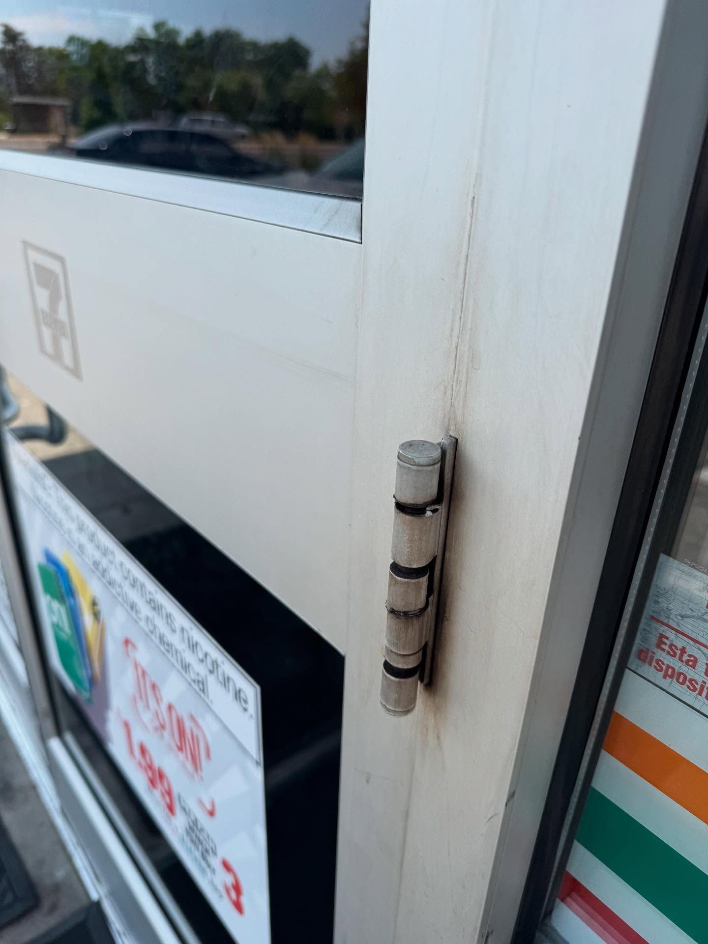 Close-up of a white door hinge on a storefront entrance with signs on the glass.