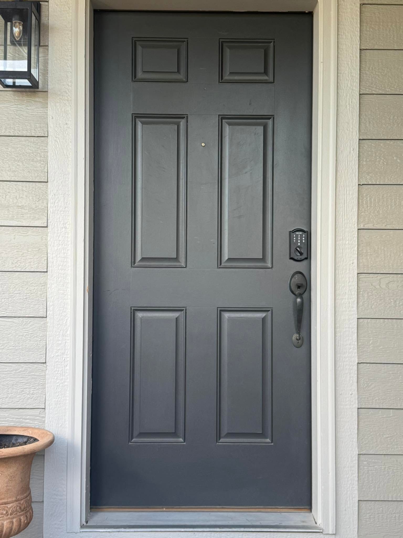 Gray front door with four raised panels, keypad lock, and handle in a stone entryway