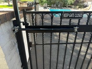 Black metal gate with a “KEEP GATE CLOSED” sign beside a concrete wall outdoors