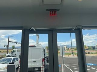 View from inside a store through glass doors to a parking lot with white van and blue sky.