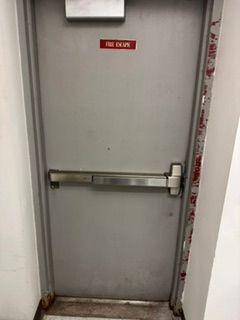 Gray metal door with a horizontal crash bar and a red “FIRE EXIT” sign